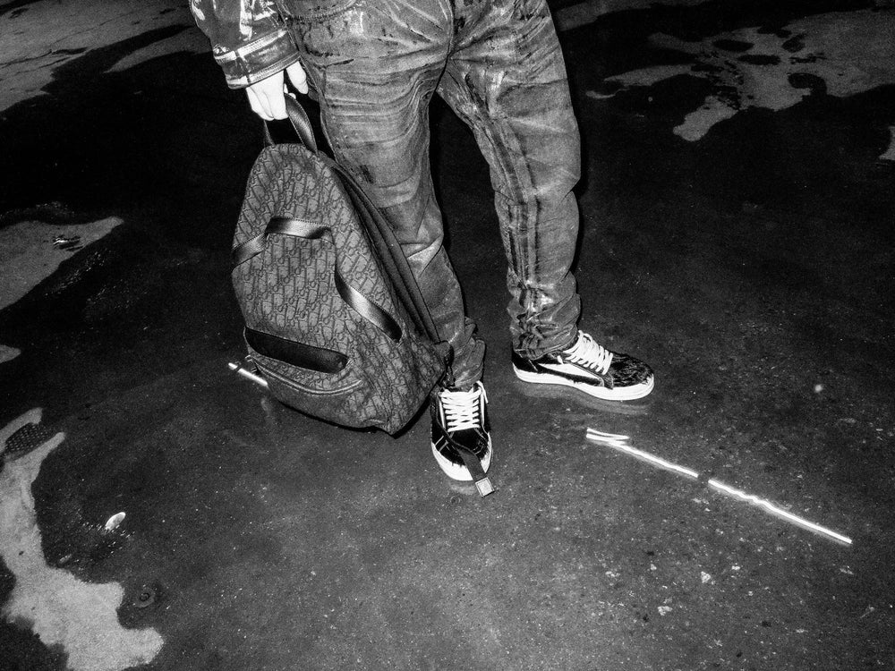 Black and white shot of sneakers and a backpack on wet pavement
